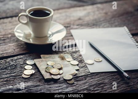 Lucidare il denaro sul tavolo, le banconote e le monete metalliche. Pezzo di carta e matita. Tazza di caffè. Foto Stock