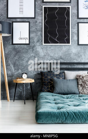 Orologio sul tavolo di legno accanto a un futon verde contro il muro di  cemento con manifesti nel buio interiore camera da letto Foto stock - Alamy