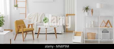 Mobili Bianchi con elementi in legno in monocromatico e living room interior con giallo poltrona, divano e foglia di monstera su un tavolo da caffè Foto Stock