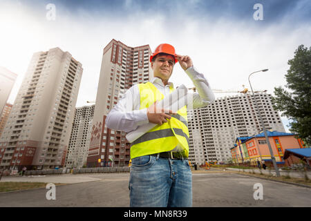 Ritratto di sorridente ingegnere maschio rosso che indossa il casco di plastica sul sito di costruzione Foto Stock