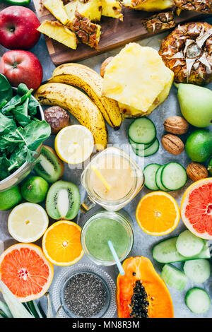 Mango sani e verde smoothie detox drink in un vetro circondato da materie frutta ingredienti,banana, ananas, papaya, cetriolo, kale,spinaci, Foto Stock