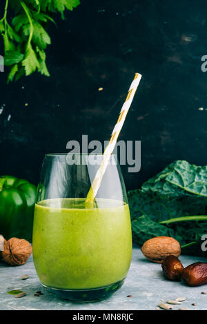 Un sano frullato verde con kalw, banana e data in vetro con golden paglia contro uno sfondo scuro. Detox, dieta, sano cibo vegetariano concept Foto Stock