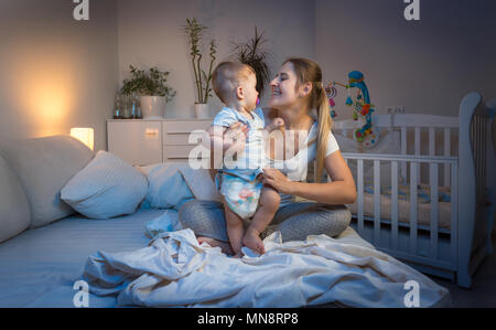 Sorridente madre modifica confuso pannolini per il suo bambino a notte Foto Stock