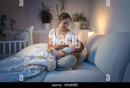 Carino 9 mesi di età Bimbo giacente sulla madre di giro e di bere latte di notte Foto Stock