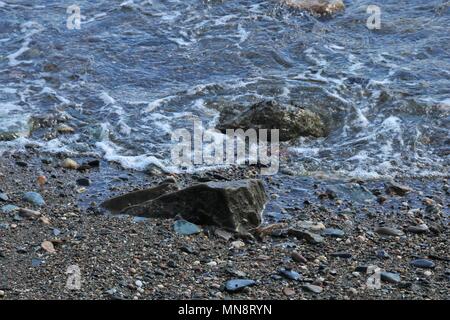 Dolce Sciabordare di onde contro le rocce di piccole dimensioni su un peddle beach in una giornata di sole. Foto Stock