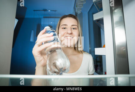 Ritratto di giovane donna bionda avete fame di prendere una bottiglia di acqua dal frigorifero durante la notte Foto Stock