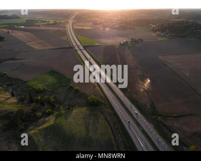 Vista aerea dell'autostrada che conduce verso il sole al tramonto con le auto in autostrada e il trattore sul campo Foto Stock