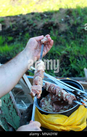 Preparazione di un shish kebab. Infilate la mano sullo spillone di pezzi di carne e cipolle. Foto Stock