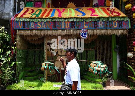 Lucban, Quezon, Filippine. Il 15 maggio 2018. Un formaggio di capra al venditore passa da una casa decorata con prodotti di origine locale. Turisti locali e stranieri accorsi a Lucban, Quezon per celebrare il 2018 Pahiyas Festival. Il festival è celebrato per rendere grazie al santo patrono della città, de San Isidro Labrador, per un abbondante raccolto. Le case sono anche adornata con frutta e verdura. Credito: SOPA Immagini limitata/Alamy Live News Foto Stock