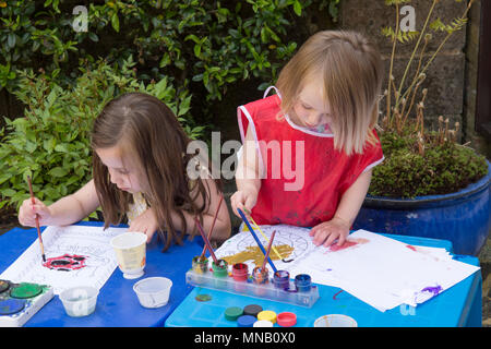 Due anni di ragazza con quattro anni di sorella, la pittura di immagini, modelli con vernici ad acquerello in giardino, ottenere vernice sulle mani. Foto Stock