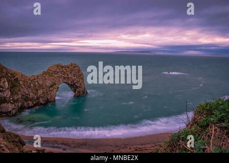 Il sole sorge oltre la Manica a Durdle porta sul Jurassic Coast in Dorset Foto Stock