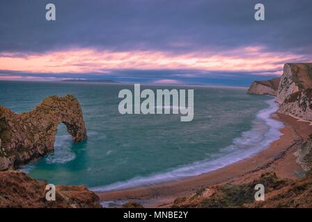 Il sole sorge oltre la Manica a Durdle porta sul Jurassic Coast in Dorset Foto Stock