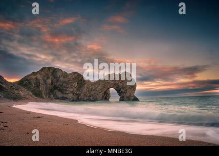 Il sole sorge oltre la Manica a Durdle porta sul Jurassic Coast in Dorset Foto Stock