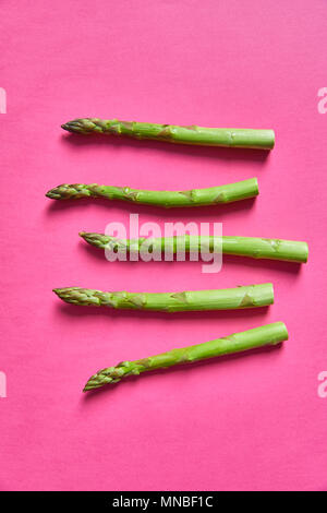 Close-up shot di cinque rametti di asparagi giacente su sfondo rosa Foto Stock