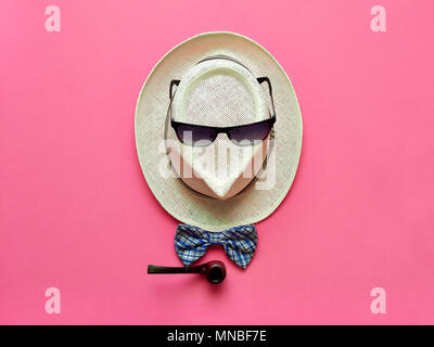Tubo di fumo e bowtie che giace vicino a cappello di paglia con occhiali da sole su sfondo rosa Foto Stock