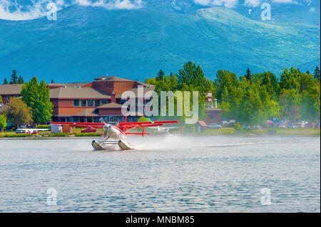 Un rosso e bianco idrovolante decolla sul lago il cofano ad Anchorage in Alaska Foto Stock