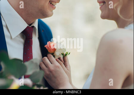 Sposa mette le mani su un boutonniere fiori su govern giacca. Foto Stock