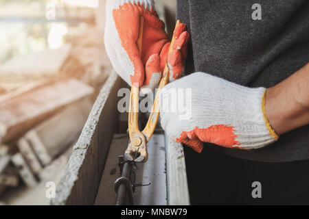 Close up dei lavoratori mani usando pinze legare il filo in acciaio per rebar prima di calcestruzzo viene riversato su di esso. Foto Stock