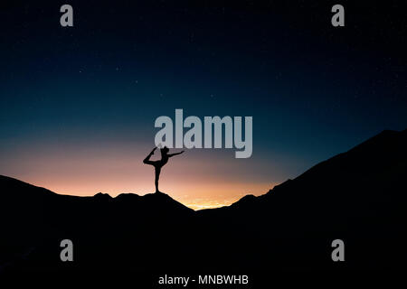 Montare l'uomo in silhouette fare yoga natarajasana pongono alla città di notte e il cielo stellato sfondo Foto Stock
