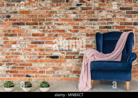 Un muro di mattoni, coperta rosa giacente sulla poltrona di colore blu Foto Stock