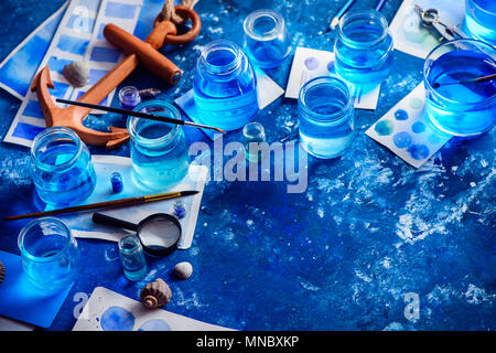 Artista creativa workplace con marine acquerello, palette campioni, spazzole e giare di acqua dall'alto. Pittura concetto del mare su un blu navy backgroun Foto Stock