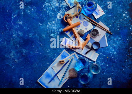 Artista workplace con schizzi ad acquerello, conchiglie, tassello di legno e bussola su uno sfondo blu scuro con copia spazio. Viaggio creativo e paintin Foto Stock