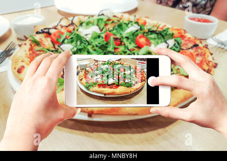 Immagine composita di fare la pizza le foto su uno smartphone - donna di mani tenendo il telefono cellulare e toccando il pulsante otturatore sullo schermo. Foto Stock