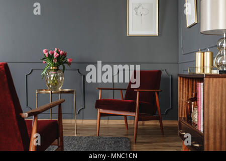 Fiori di colore rosa sulla tavola d'oro accanto al rosso poltroncina in legno scuro in living room interior Foto Stock