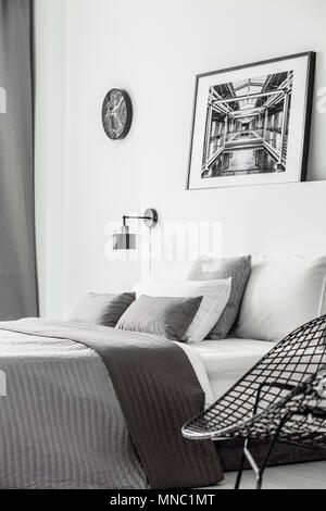 Biancheria da letto grigio sul letto in camera da letto moderno interno con poster su bianco testata vicino a un orologio Foto Stock