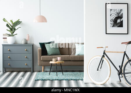 Bicicletta e poster in accogliente soggiorno interno con un tavolo di legno vicino al lettino di marrone e grigio armadietto Foto Stock