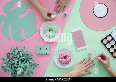Ragazze chiodi di pittura su una rosa e tavolo verde con ciambelle e pianta Foto Stock