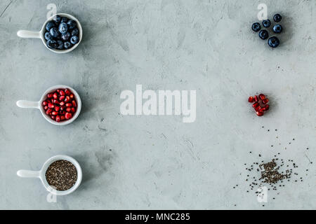 Vista dall'alto di una disposizione simmetrica dei mirtilli, melograno e semi su una tabella di colore grigio. Foto Stock