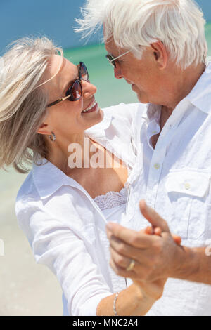 Felice senior l uomo e la donna coppia danzante e tenendo le mani su una deserta spiaggia tropicale con mare turchese e cielo blu chiaro Foto Stock