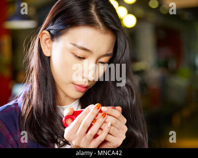 Bella giovane donna asiatica guardando una tazza di caffè con grave l'espressione del viso. Foto Stock