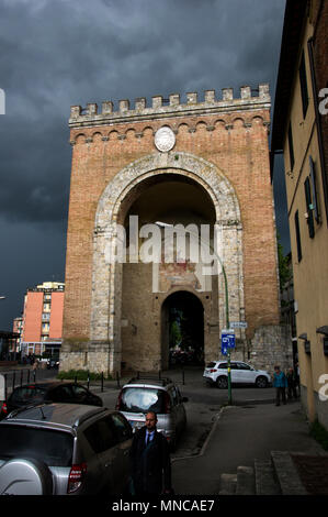 Antiporto di Camollia gate per inserire la città di Siena, Italia con un moody scuro cielo tempestoso dietro di essa e la luce del sole sull'ingresso Foto Stock