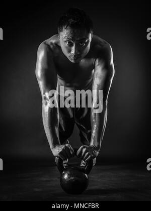 Foto di un muscoloso uomo asiatico facendo pushups con un kettlebell. Focus sul suo volto. Foto Stock