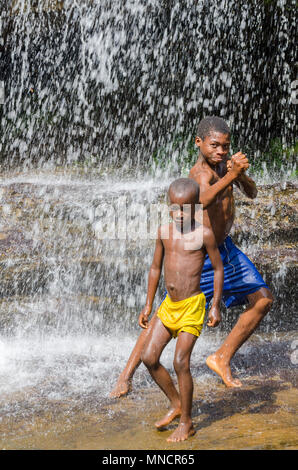 Kindia, Guinea - Dicembre 28, 2013: non identificato due giovani ragazzi africani wplaying e divertirsi sotto la cascata Foto Stock