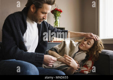 Uomo che guarda la pillola blister durante la seduta da uno stato di malessere donna sdraiata sul divano di casa Foto Stock