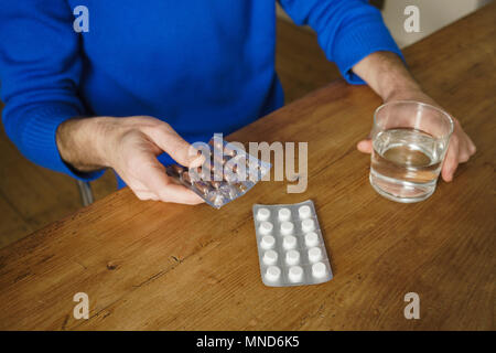 Sezione mediana dell'uomo prendendo medicine con acqua a tavola Foto Stock