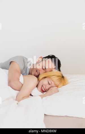 Sorridente amare giovane che dorme sul letto contro la parete a casa Foto Stock
