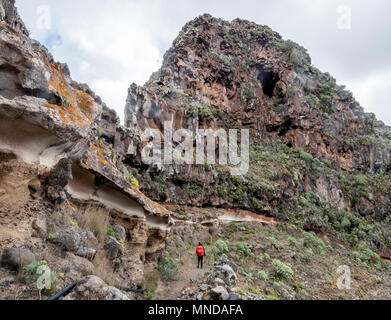 Walker passando curiosamente weathered soft di pomice bianca sotto lo strato duro strati di basalto sopra San Sebastian su La Gomera Canarie Foto Stock