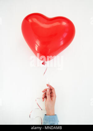 Donna di mano che regge un cuore rosso palloncino. Il giorno di San Valentino biglietto di auguri. Bianco sullo sfondo di vacanza. Vista dall'alto. Ti amo concept Foto Stock