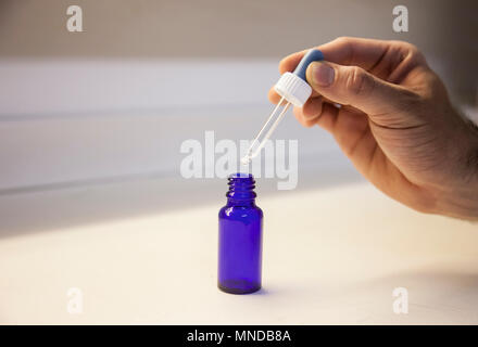 Medicina dropper in mano con un po' di bottiglia blu Foto Stock