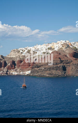Vista acqua guardando la comunità greca di Oia, con case e la collina e la piccola barca in mare Foto Stock