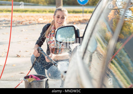 Donna con ugello alta pressione per pulire la sua vettura Foto Stock