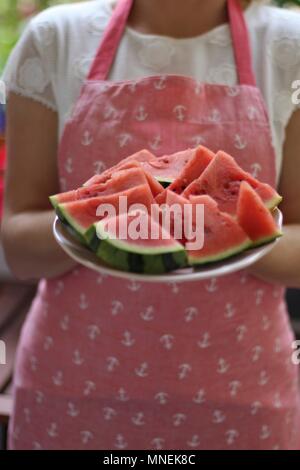 Una donna che indossa un grembiule tenendo un piatto di fette di melone Foto Stock