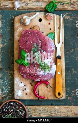 Carne di maiale cruda con erbe aromatiche, aglio, pepe e peperoncino su un tagliere Foto Stock