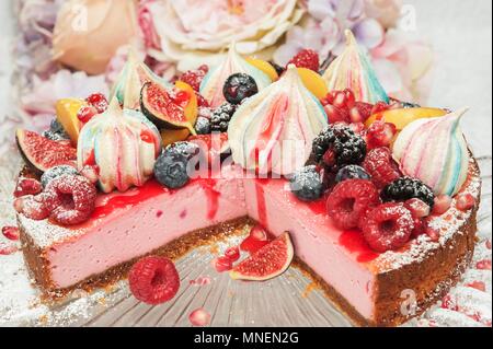 Strawberry Cheesecake con merangue baci e frutta fresca sulla parte superiore su una torta di vetro a stare di fronte di fiori Foto Stock