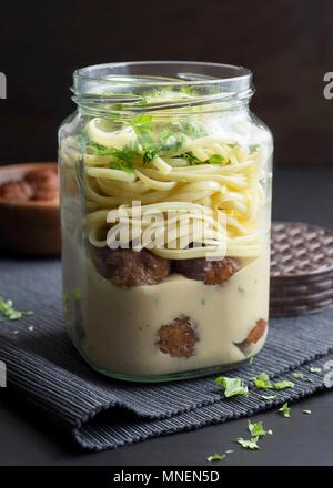 Le polpette di carne e tagliatelle in un vasetto di vetro con crema a base di soia e di prezzemolo fresco Foto Stock