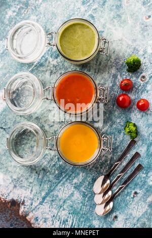 Varie zuppe colorate in vasetti di vetro (zuppa di broccoli zuppa di pomodoro, zuppa di zucca) Foto Stock